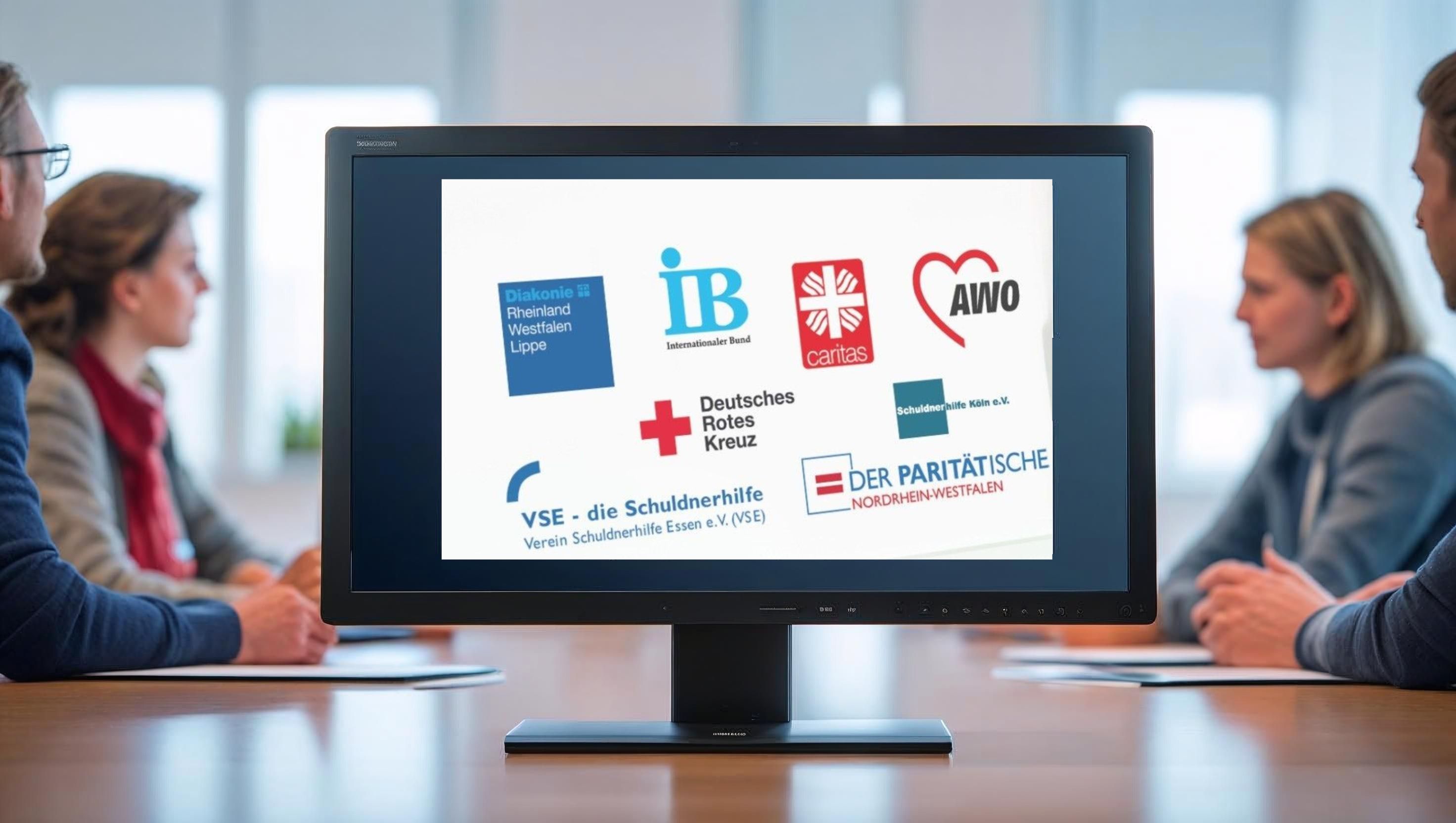 In einem Meeting Raum steht ein Monitor, auf dem Logos dargestellt sind.